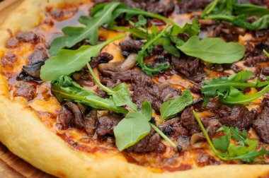 Tahta üzerinde biftek, fesleğen, peynir, yeşillik ve domates soslu İtalyan pizzası.