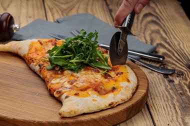 Erkek eli tahta tahtada Calzone pizzası kesiyor.