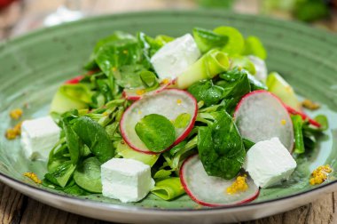 Yeşillik, yumuşak peynir ve ahşap masada dilimlenmiş turplu taze ve lezzetli bir salata.
