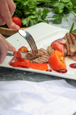 Taze domatesli, biberli, soğanlı ve soslu ızgara domuz etinin tadına bakmak için çatal ve bıçak kullanan kadın elleri