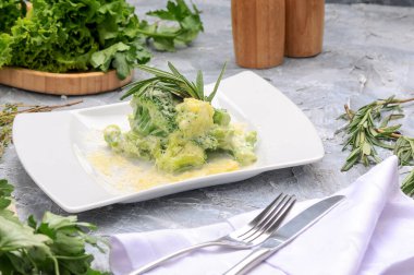 Parmesan peynirli yeşil brokoli ve beyaz tabakta biberiye yaprakları.