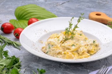 Lezzetli makarna, krem peynir ve beyaz tabakta bitkiler.