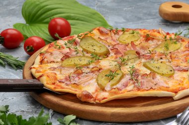 Domuz pastırmalı, peynirli ve tahta üzerinde salatalık turşulu pizza.