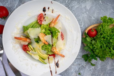 Beyaz tabakta taze salata, karides, domates, marul ve parmesan peyniri.