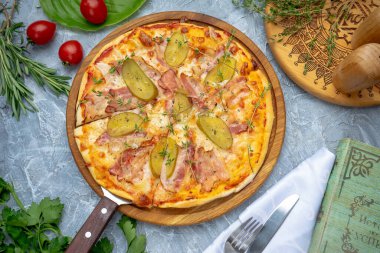 Domuz pastırmalı, peynirli ve tahta üzerinde salatalık turşulu pizza.