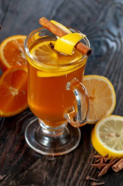 Dilimlenmiş limonlu çay bardağı, portakal ve ahşap yüzeyde tarçın çubukları.