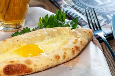 Tahtanın üzerinde yumurta sarısı ve masada bir bardak bira olan khachapuri.