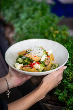 Salata tabağı taşıyan kadının yakından görünüşü rulo ve yeşillik içerir.