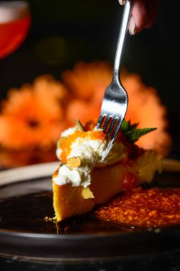 Tao yağında lezzetli balkabağı peynirli kek tatmak için çatal bıçak kullanan kadın elleri, arka planda gerbera çiçekleri.