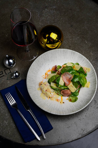 блюдо из вкусного салата с ветчиной, сыром и вкусным соусом с красным бокалом вина