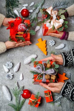 Gri arka planda hediyelerle süslenmiş insanların elleri.