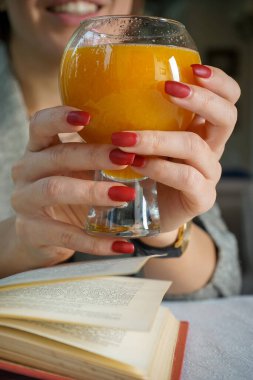Kadın kitap okurken portakal suyu içiyor.