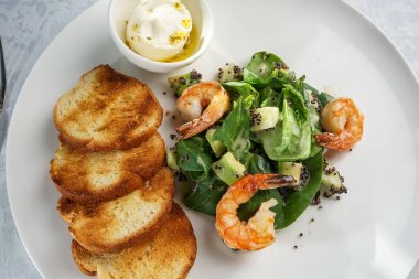 healthy breakfast of poached egg, shrimp salad and bruschetta on white plate 