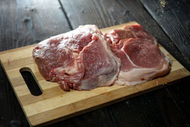 Tahta kesme tahtasında tuzlu ve biberli çiğ domuz bifteği. 