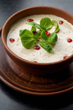 Bir kase lezzetli çorba ve masada yeşillik.