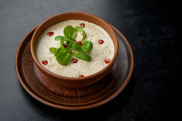 Bir kase lezzetli çorba ve masada yeşillik.