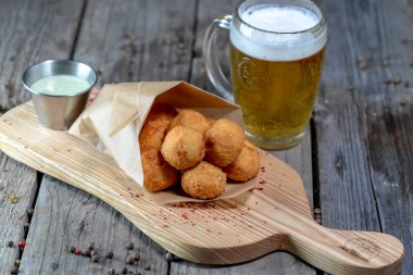 Sos, kızarmış peynir topları ve tahta arka planda bira.