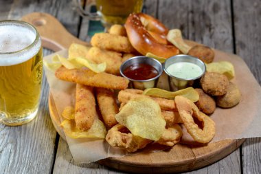 Bir tabak cips, ahşap masada biralı peynir çubukları. 