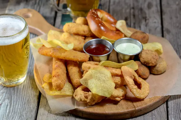 Bir tabak cips, ahşap masada biralı peynir çubukları. 