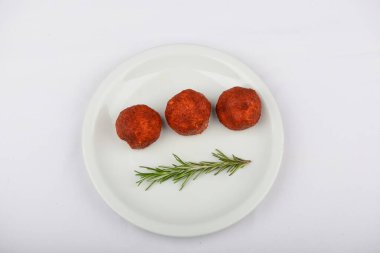 Beyaz tabakta biberiye dalıyla servis edilen baharatlı yuvarlak aperatifler.