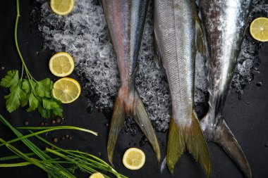 Siyah arka planda otlar ve dilimlenmiş limonlu üç balık.