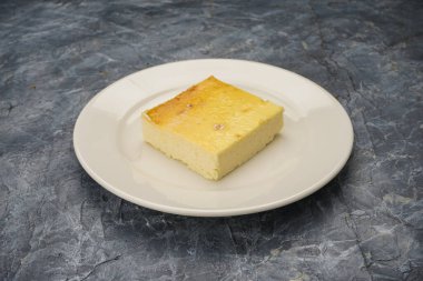 Beyaz tabakta kare şeklinde cheesecake..