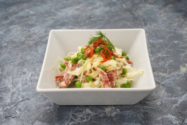 Lahanalı salata, bezelye, salam ve otlar beyaz kasede..