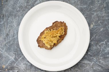 Kızarmış soğanlı domuz bifteği, beyaz tabakta..