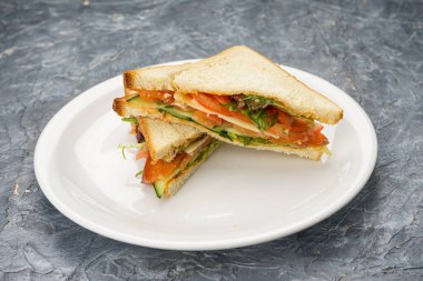 Sandviç, beyaz tabakta sebzelerle üçgen şeklinde kesilmiş..