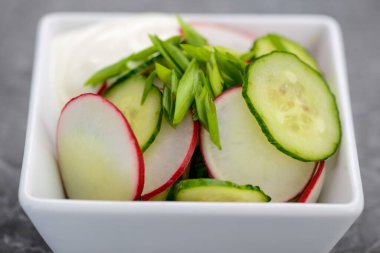 Dilimlenmiş turp, salatalık ve taze soğandan oluşan sağlıklı bir salata, kremalı sosla servis edilir..