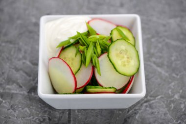 Dilimlenmiş turp, salatalık ve taze soğandan oluşan sağlıklı bir salata, kremalı sosla servis edilir..