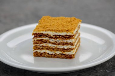 Beyaz bir tabakta servis edilen kremalı çok katmanlı ballı bir pasta..