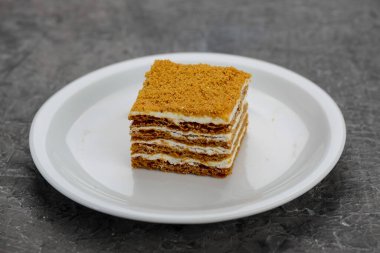 Beyaz bir tabakta servis edilen kremalı çok katmanlı ballı bir pasta..