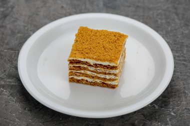 Beyaz bir tabakta servis edilen, kremalı, çok katmanlı tek bir dilim ballı kek..