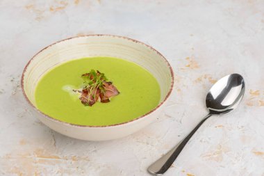 Bir kase yeşil bezelye kremalı çorba ve bir garnitür dolusu çıtır pastırma ve otlar..