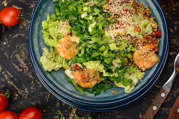 Mavi tabakta karides, yeşillik ve susam tohumlu büyük bir salata..