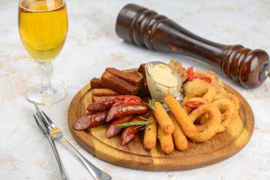 İçinde soğan halkaları, kanatlar, sosis ve bir bardak bira bulunan çeşitli bar atıştırmalıkları olan ahşap bir tabak..