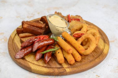İçinde soğan halkaları, kanatlar, sosis ve sosis bulunan çeşitli bar atıştırmalıkları olan ahşap tabaklar..