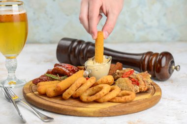 Bir insanın eli, kızarmış bir atıştırmalığı ahşap bir tabakta sos kasesine daldırıyor..