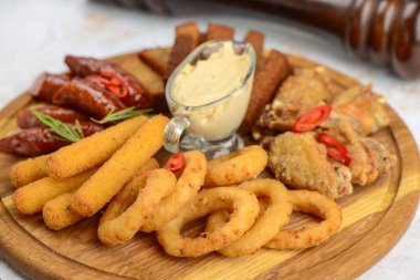 İçinde soğan halkaları, kanatlar, sosis ve sosis bulunan çeşitli bar atıştırmalıkları olan ahşap tabaklar..