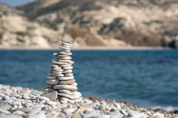 Stones pyramid on background of Mediterranean sea. Seashore background with stone tower. Tower of rocks on beach. Small Zen out of pile of stones on rock. Aphrodite beach in Cyprus.