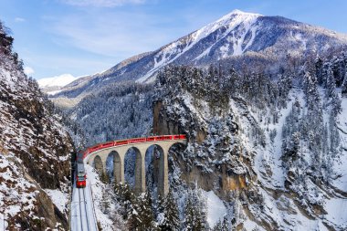 Filisur, Switzerland - January 10, 2024: Rhaetian Railway passenger train at the famous Landwasser Viaduct on Albula line by Stadler Rail in the Swiss Alps in Filisur, Switzerland. clipart