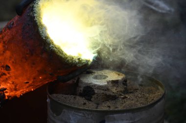 Kızgın alevler ve dumanla birlikte kızgın çömlekten sıvı metal döküyorlar.