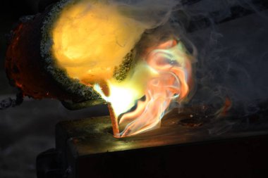 Kızgın alevler ve dumanla birlikte kızgın çömlekten sıvı metal döküyorlar.