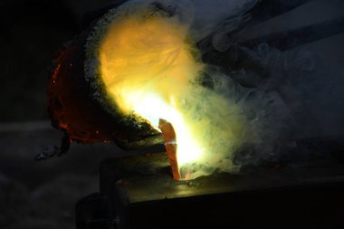 Kızgın alevler ve dumanla birlikte kızgın çömlekten sıvı metal döküyorlar.