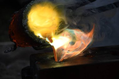 Kızgın alevler ve dumanla birlikte kızgın çömlekten sıvı metal döküyorlar.