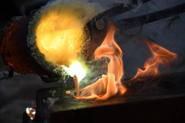 Kızgın alevler ve dumanla birlikte kızgın çömlekten sıvı metal döküyorlar.