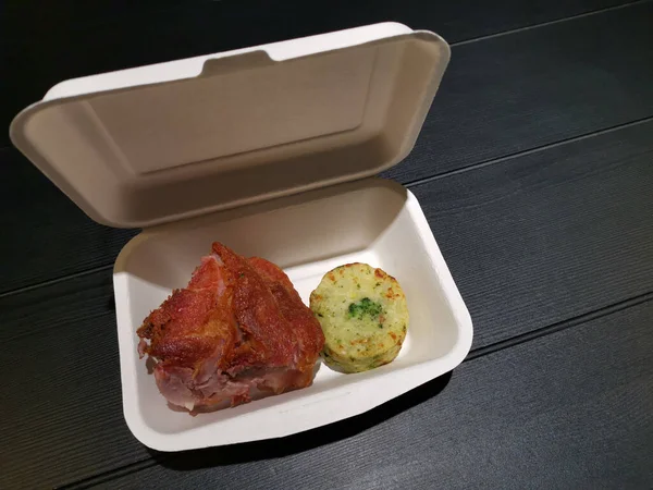 paper meal box filled with fried pork and cooked potato and spinach on black table with copy space
