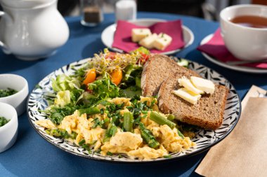 Çırpılmış yumurta, sebze, kuşkonmaz, tost, soğan, tohum filizi ve sebzeler güzel dekore edilmiş bir tabakta servis edilir, kahvaltı seti, sabah güneşiyle aydınlatılır..