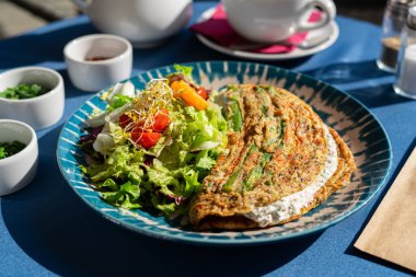 Süzme peynirli omlet ve taze sebzeler güzel mavi ve beyaz bir tabakta servis edilir. Sabah güneşiyle aydınlatılan bir kahvaltı seti.
